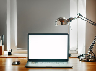 Laptop computer with blank white screen on wooden desk. The home workplace.