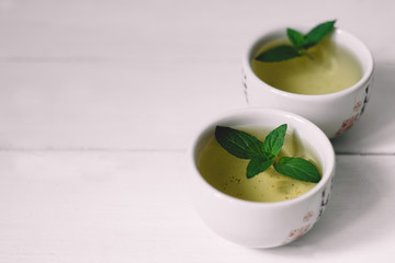 two mugs of green tea with mint on a white table