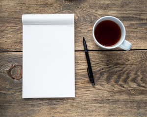 tea Cup, pencil or pen and open Notepad with a clean white page on wooden table, top view