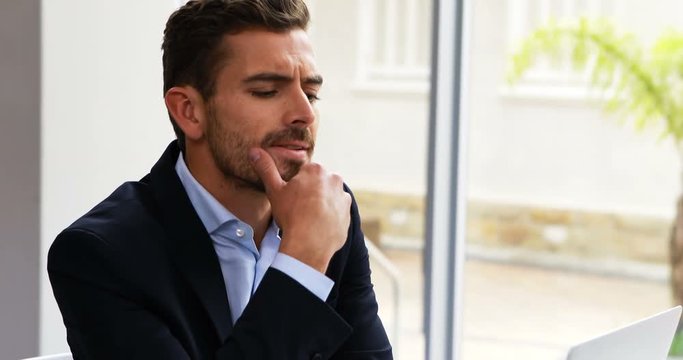 Thoughtful businessman working on laptop at desk 