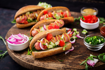 Hot dog with cucumber, tomato and red onion on wooden background.