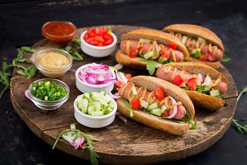 Hot dog with cucumber, tomato and red onion on wooden background.