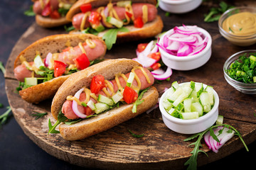 Hot dog with cucumber, tomato and red onion on wooden background.