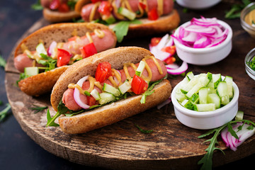 Hot dog with cucumber, tomato and red onion on wooden background.