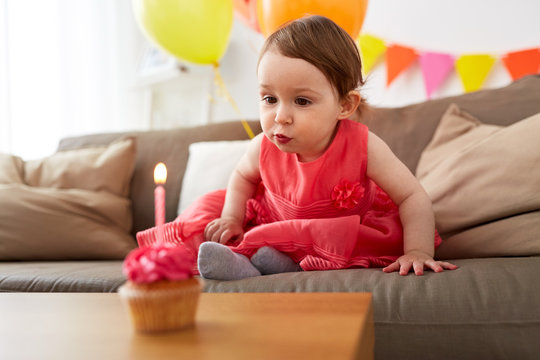 girl blowing to candle on birthday cupcake at home