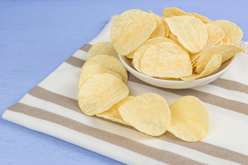 crispy potato chips on cotton fabric with light blue wooden background, close up