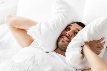 man in bed with pillow suffering from noise