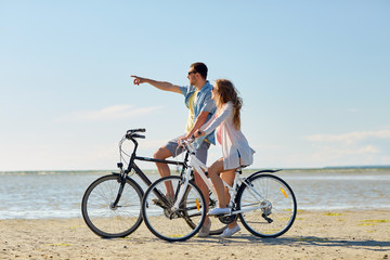 happy young couple riding bicycles at seaside