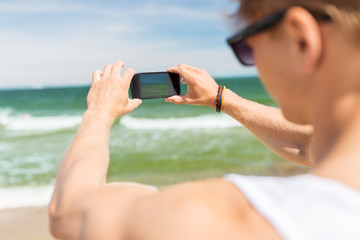 man with smartphone photographing on summer beach