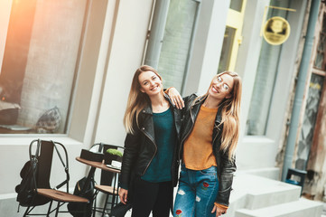 It is funny walk with best friend! Two beautiful women walking outdoor hugging and laughing on autumn street. Fashion urban girls spending weekend talking at sunset near a cafe. Friendship, beauty.