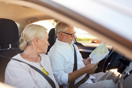 happy senior couple with map driving in car