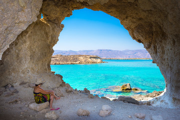 Amazing summer view of woman in a cave at Koufonisi island with magical turquoise waters, lagoons,...
