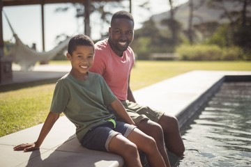 Smiling father and son sitting on edge of swimming pool