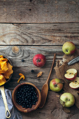 Forest harvest: blueberry, apples and chanterelle mushrooms on gray rustic background with a piece of linen cloth. Autumn nature concept. Top view with copy space in upper part.