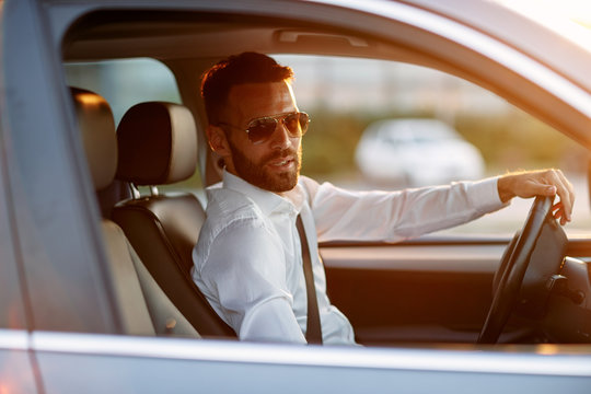 Stylish businessman wearing sunglasses while driving car.