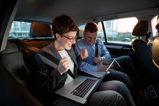 Businesspeople looking at laptop in car on trip.
