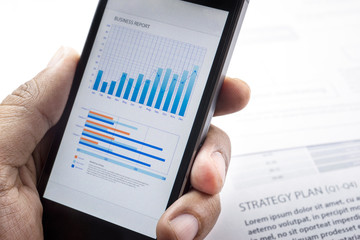 Close up of  businessman hand holding smartphone with business graph chart background. business analysis concept.