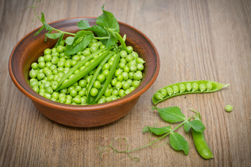 Fresh green peas in a clay bowl on a wooden table