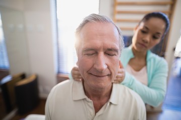 Senior male patient with eyes closed receiving neck massage from