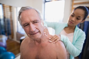 Shirtless male patient receiving neck massage from female
