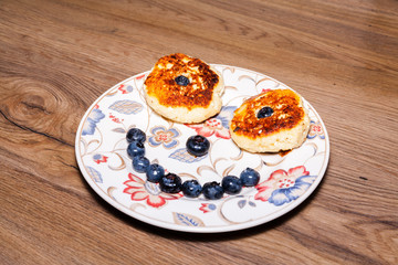 bowl with flowers full of fresh curd pancakes with blueberries. On wood table