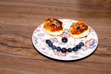 bowl with flowers full of fresh curd pancakes with blueberries. On wood table