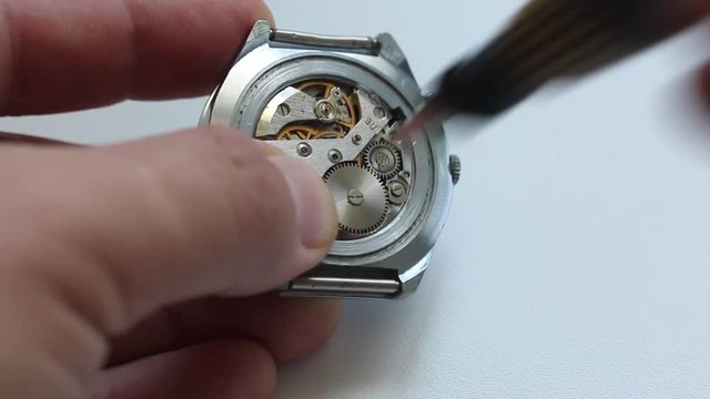 Watchmaking is a master at work. Disassembles the clock using a screwdriver. Repair of old watches. The mechanism of the clock, the screwdriver, which the master makes repairs, is visible