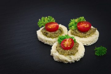 finger food for party Homemade Canape pesto sauce on top tomato and parsley leaf on black slate plate