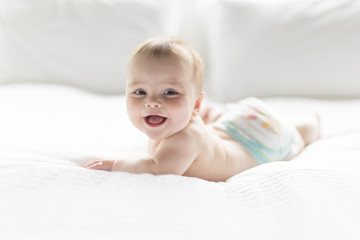 Cute happy 7 month baby girl in diaper lying and playing - obrazy, fototapety, plakaty