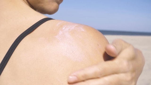 Woman applying sun lotion on her shoulders. Woman applying sun block cream on the beach.