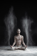 Sporty serene young man meditating sitting in cross-legged yoga lotus pose, Padmasana with palms in mudra