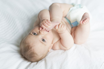 Cute happy 7 month baby girl in diaper lying and playing - obrazy, fototapety, plakaty
