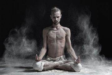Sporty serene young man meditating sitting in cross-legged yoga lotus pose, Padmasana with palms in...
