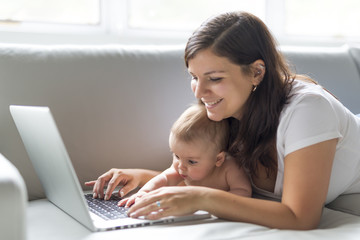 mother and baby child are looking to play and read computer on the couch at home