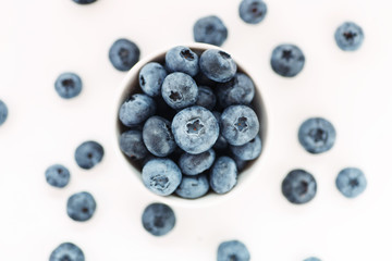 Heap of fresh ripe blueberries in a white ceramic bowl on a white background, top view, shallow depth of field