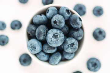 Heap of fresh ripe blueberries in a white ceramic bowl on a white background, top view, shallow depth of field, macro shot