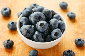 Fresh ripe blueberries in a white bowl on a wooden board, closeup shot