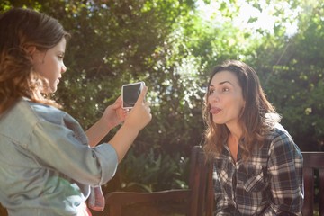Fototapeta premium Side view of girl photographing mother sticking out tongue