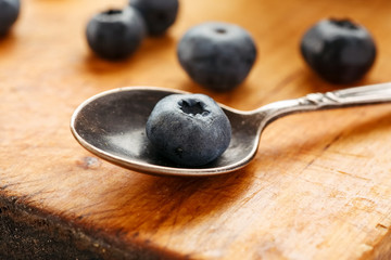 Big fresh ripe blueberry in a metal spoon on a wooden table, closeup shot