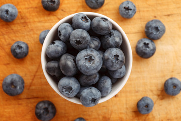 Fresh ripe blueberries in a white bowl on a wooden board, closeup shot, top view