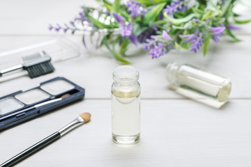 Cosmetic eyeshadow with brushes, two small glass bottles with liquid inside and lavender flower on a white wooden table