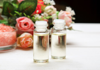 Two glass vials with liquid inside and rose flowers behind on a white wooden table, closeup shot