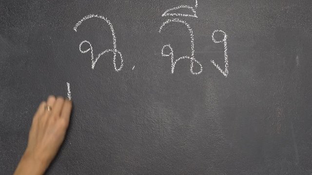 Woman's hand writing Thai letter "ฉ" with white chalk on blackboard