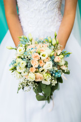 Close up of incognito bride in beautiful wedding dress holding colorful blooming bouquet of flowers. Blue, white, green, orange wedding flower. Special day of woman life.