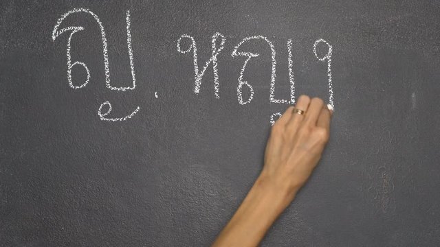 Woman's hand writing Thai letter "ญ" with white chalk on blackboard