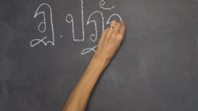 Woman's hand writing Thai letter "ฏ" with white chalk on blackboard