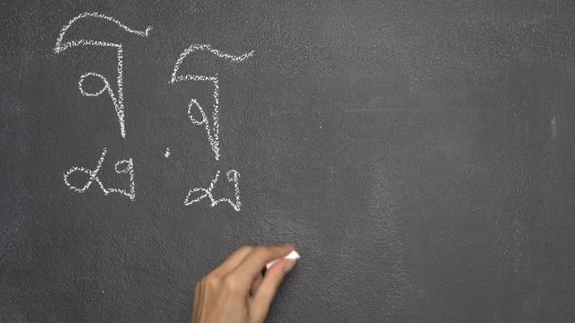 Woman's hand writing Thai letter "ฐ" with white chalk on blackboard