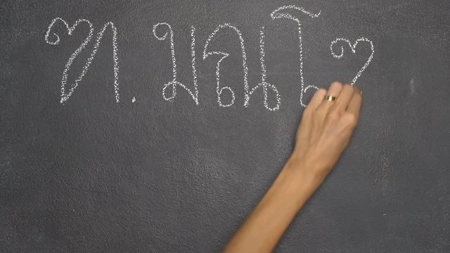 Woman's hand writing Thai letter "ฑ" with white chalk on blackboard