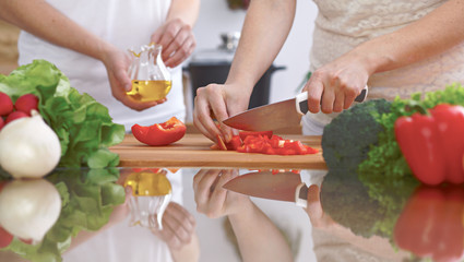 Close-up of four human hands are cooking in a kitchen. Friends having fun while preparing fresh salad. Vegetarian, healthy meal and friendship concept