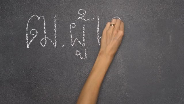 Woman's hand writing Thai letter "ฒ" with white chalk on blackboard
